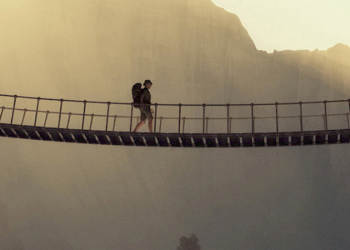 Mann mit Rucksack geht über eine Hängebrücke - © 